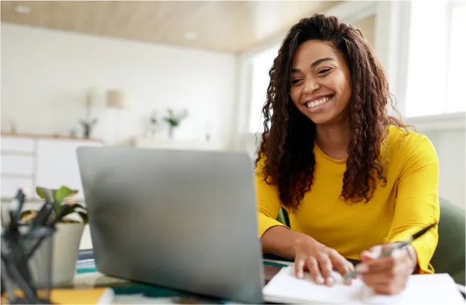 Woman smiling at a computer while taking notes