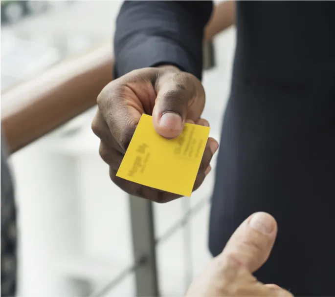 Close up of a person handing a yellow business card to another person