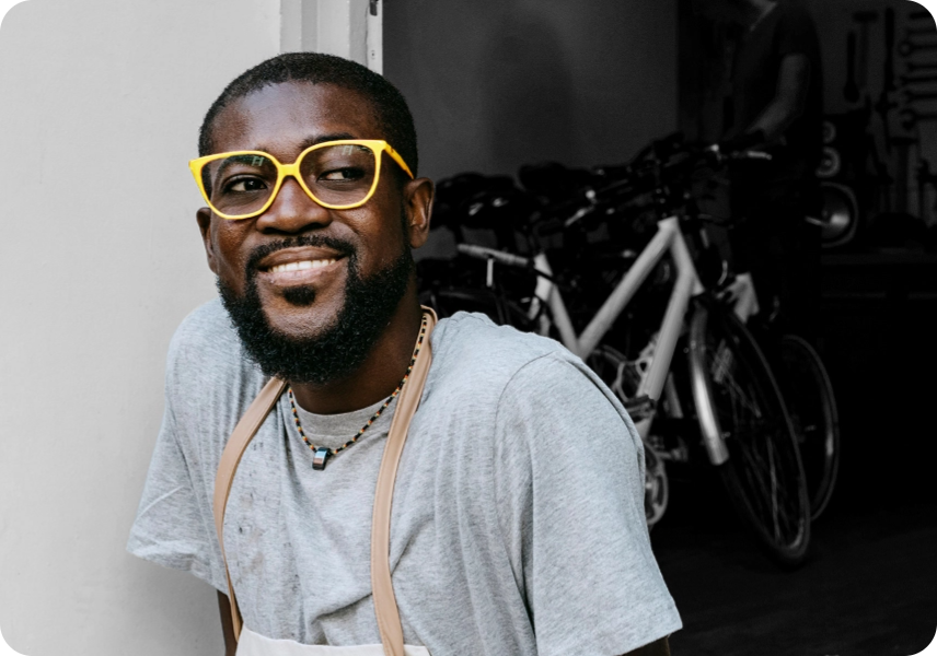 A man in front of his bike shop wearing glasses and an apron